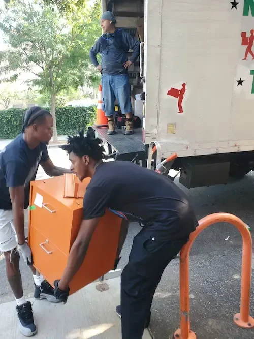 Professional movers loading an orange filing cabinet into a moving truck