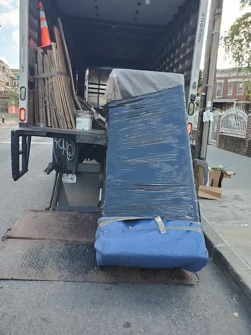 NYC Brooklyn Movers LLC crew loading a wrapped couch onto a moving truck