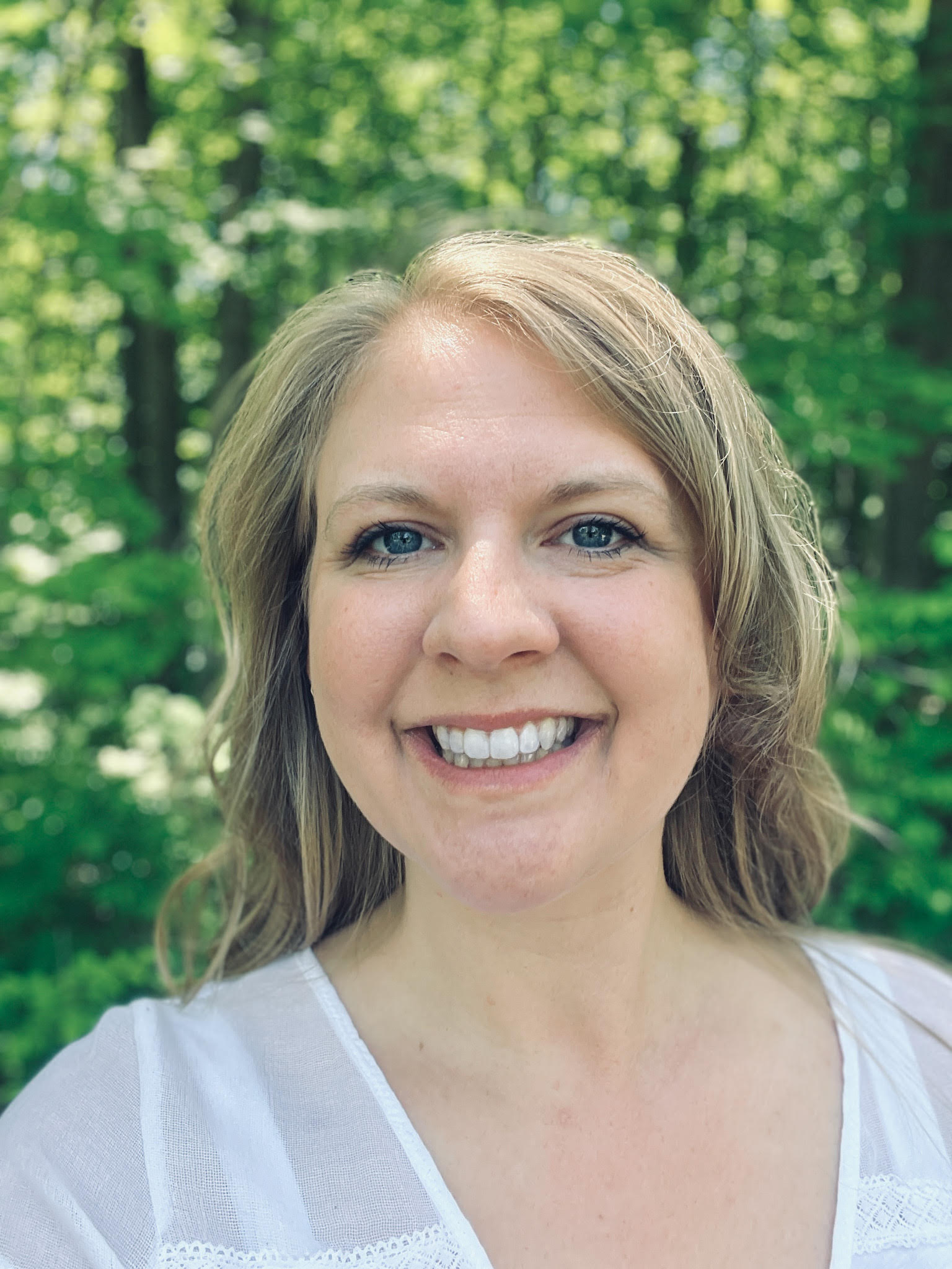 Dr. Hanah Stiverson smiling outdoors in front of green foliage.