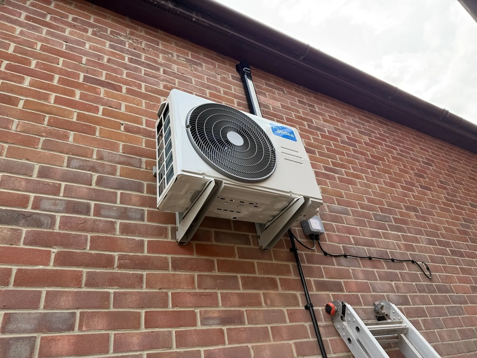 Midea outdoor unit mounted on wall brackets with black pipework trunking in Fareham
