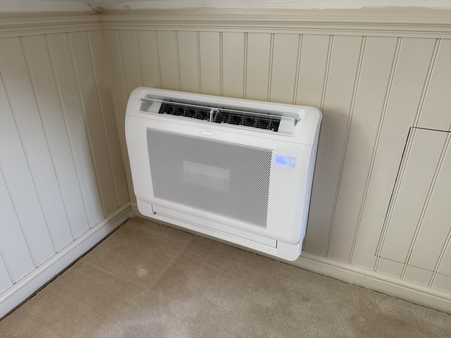 Floor-mounted air conditioning console beneath wall panelling