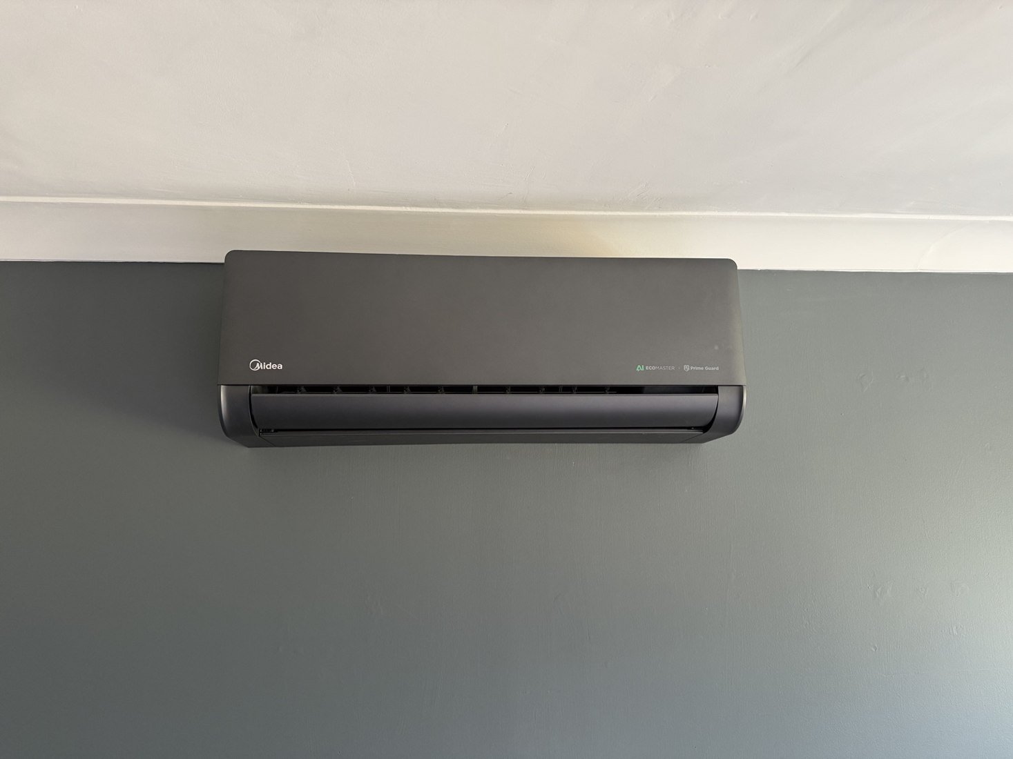 Dark grey wall-mounted air conditioning unit on a grey wall