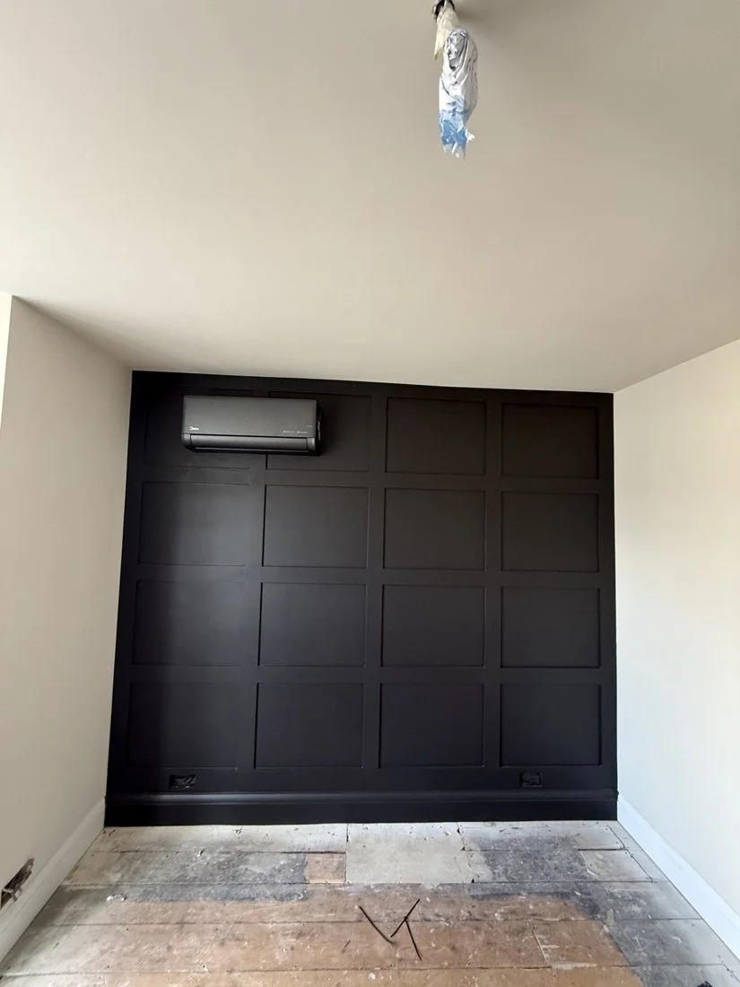 Dark wall-mounted air conditioning unit above black wall panelling