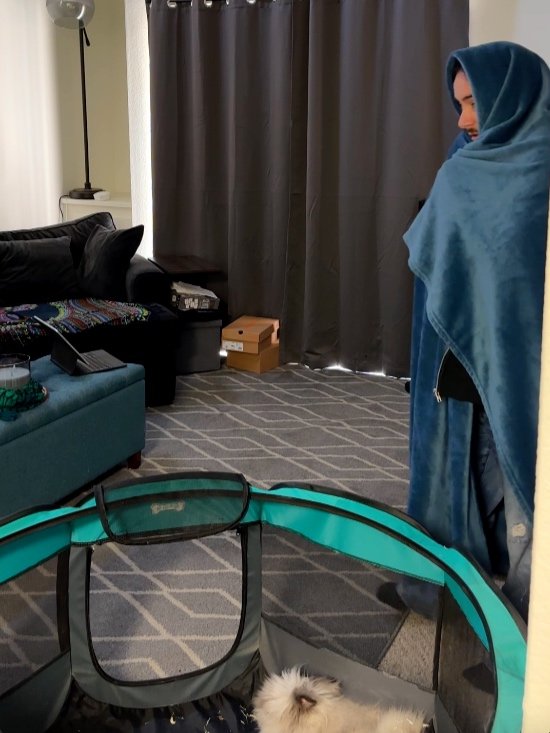 Man wrapped in blue blanket watching rabbit inside teal playpen—cozy home vibe.