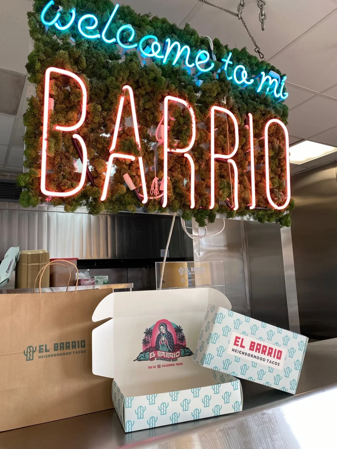 El Barrio neon sign above branded takeaway boxes and a paper bag