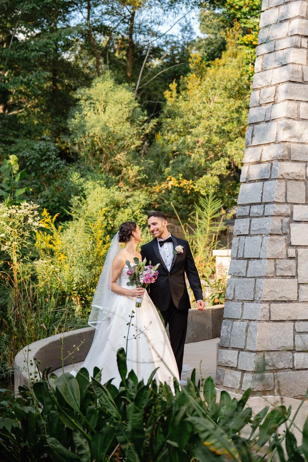 Newlyweds sharing a smile beside a stone column