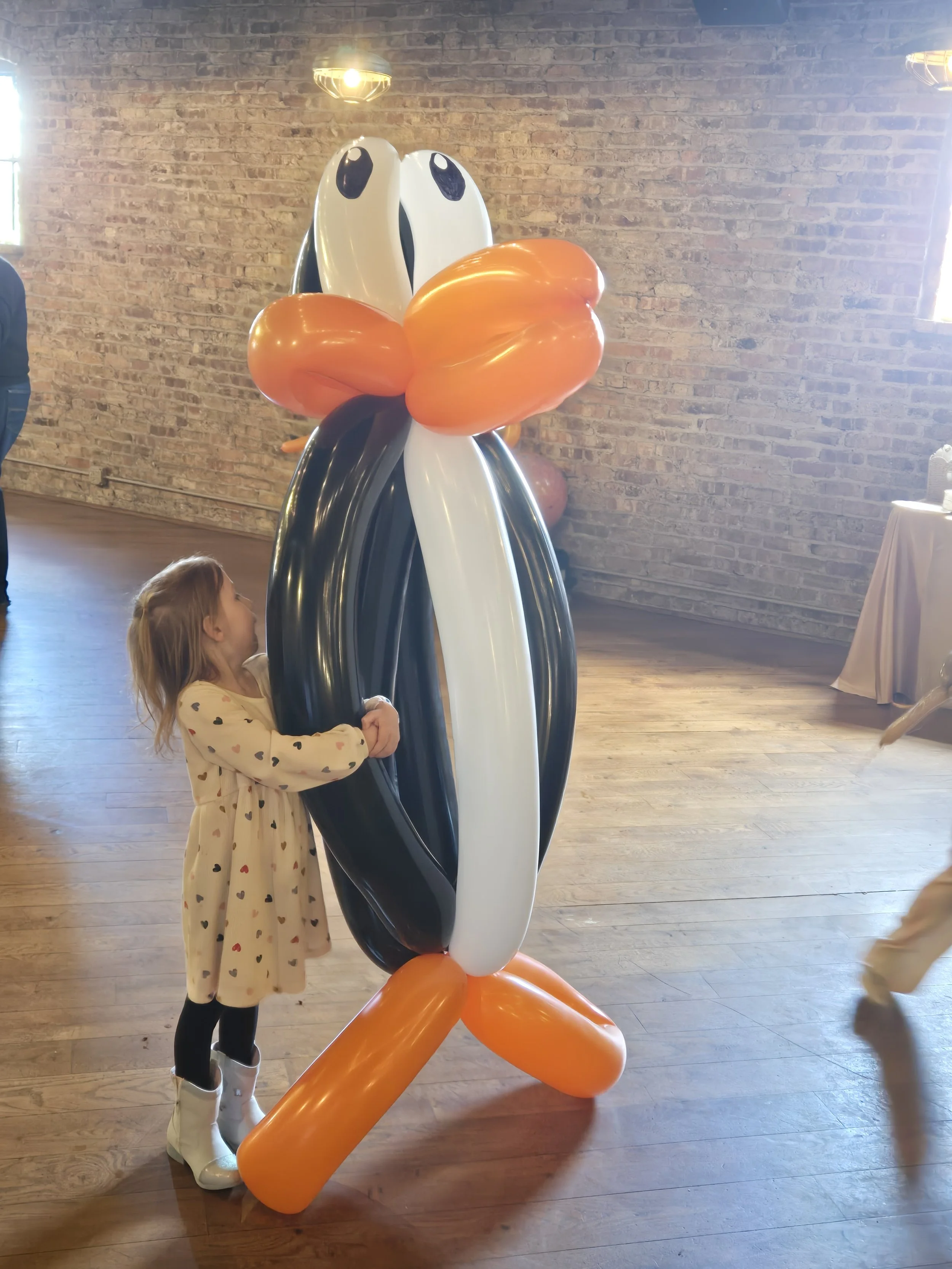 Toddler hugging a giant balloon penguin sculpture
