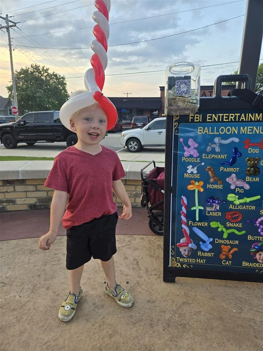 Boy in a balloon hat next to the FBI Entertainment balloon menu