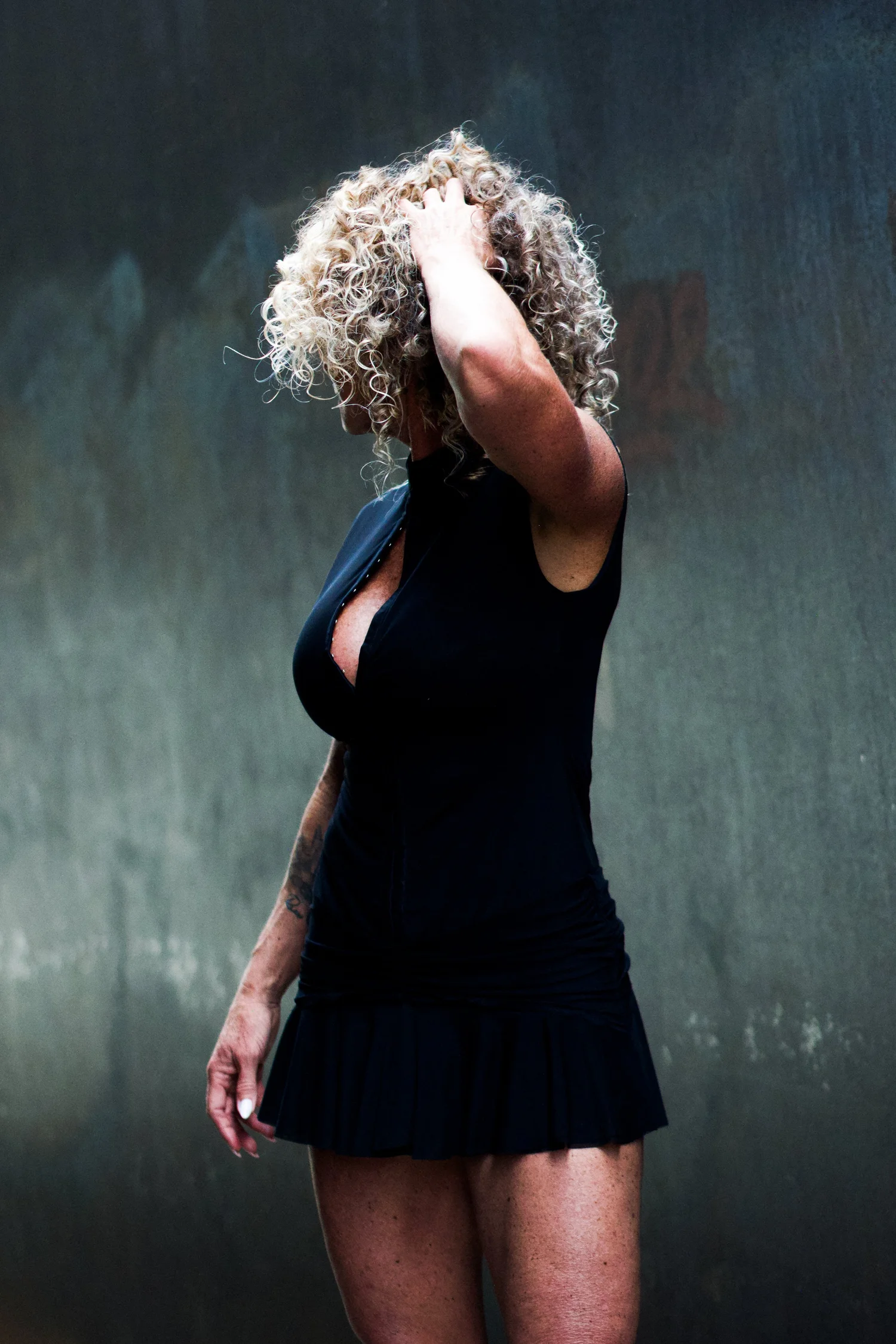 Chrisanna with one hand in her curls, eyes closed, against a steel wall