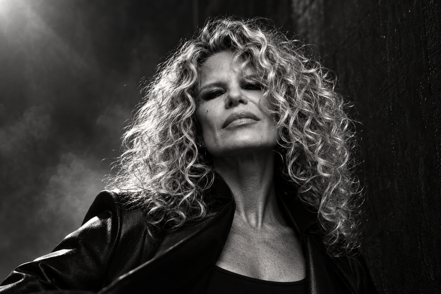 Chrisanna in a black leather coat, shot from below through smoke, curls lit from behind