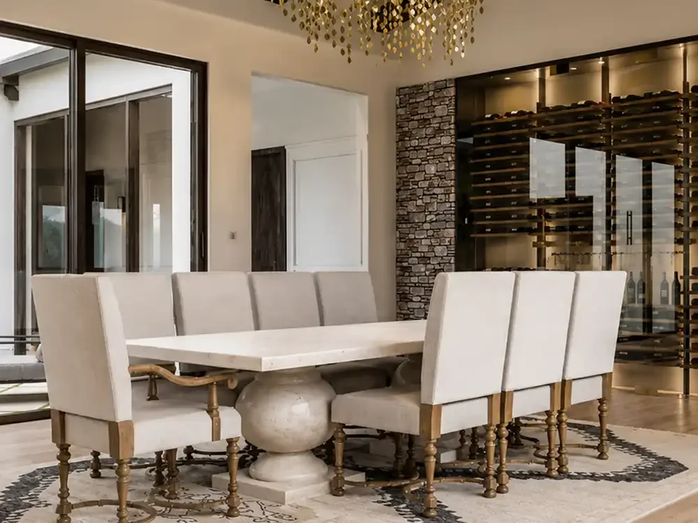 Elegant residential dining room with upholstered chairs, statement lighting, and a glass-enclosed wine display