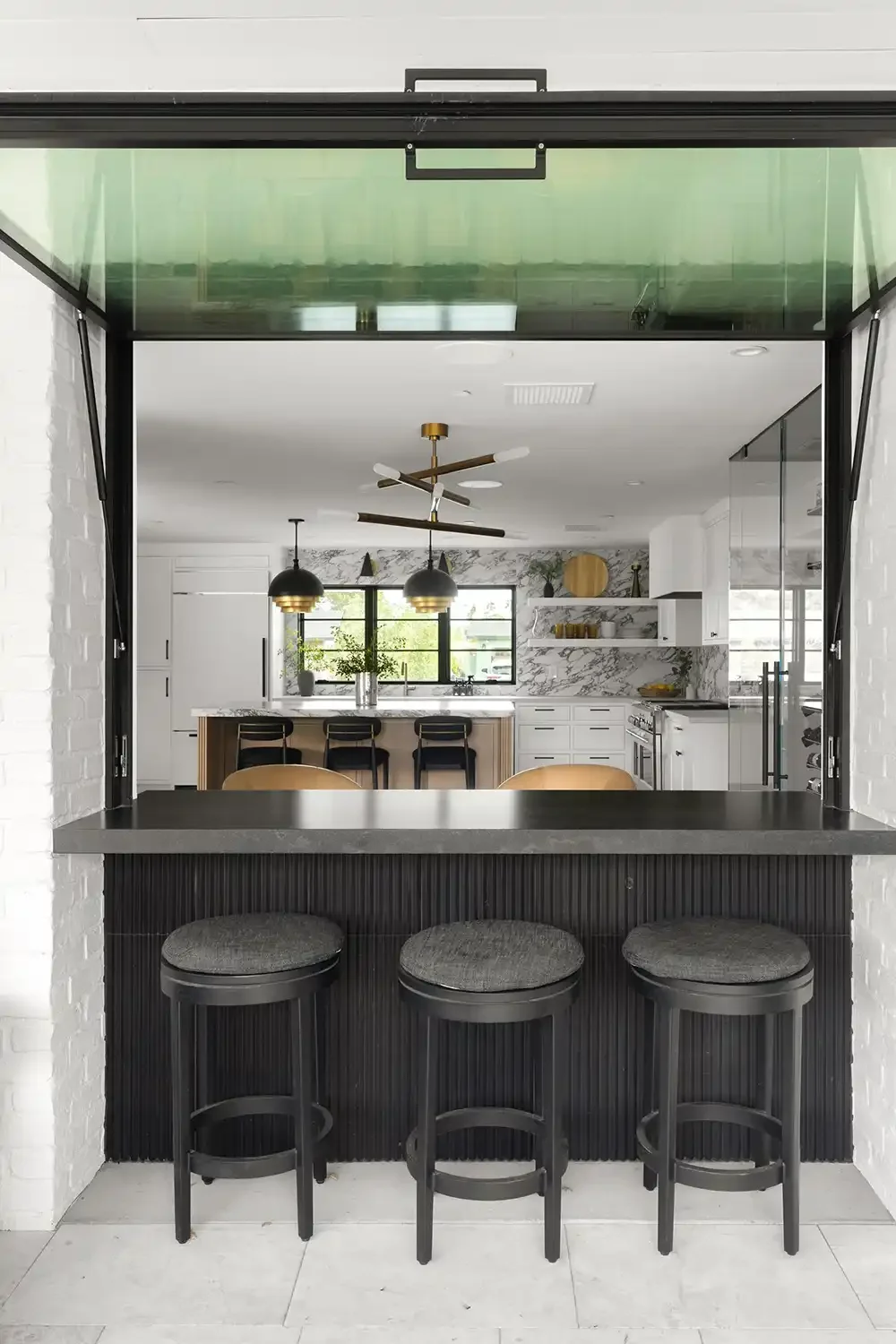 Outdoor bar with three stools beneath an open awning window into a kitchen