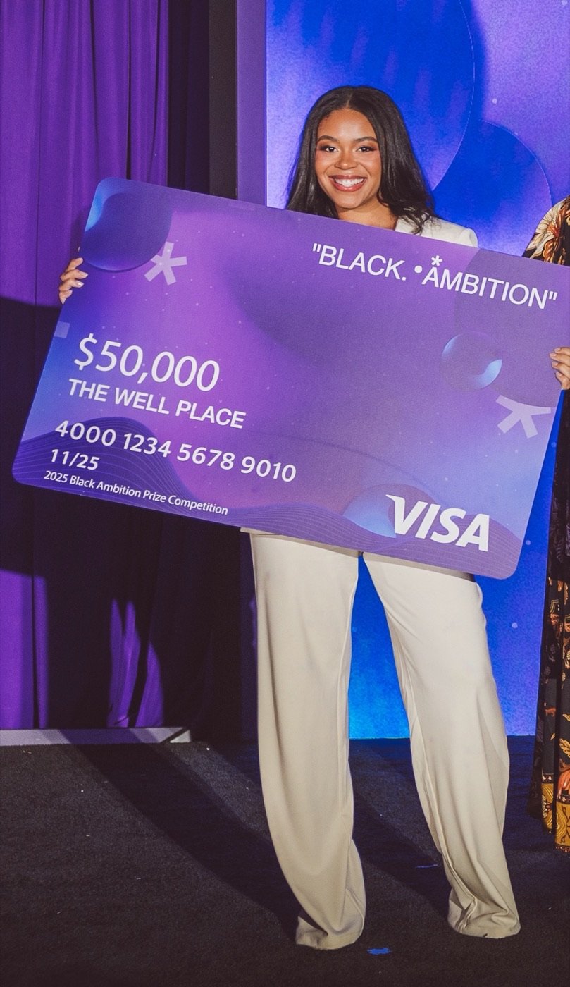 Kaylan K. Jackson, PhD, on stage holding The Well Place's $50,000 Black Ambition Prize, November 2025