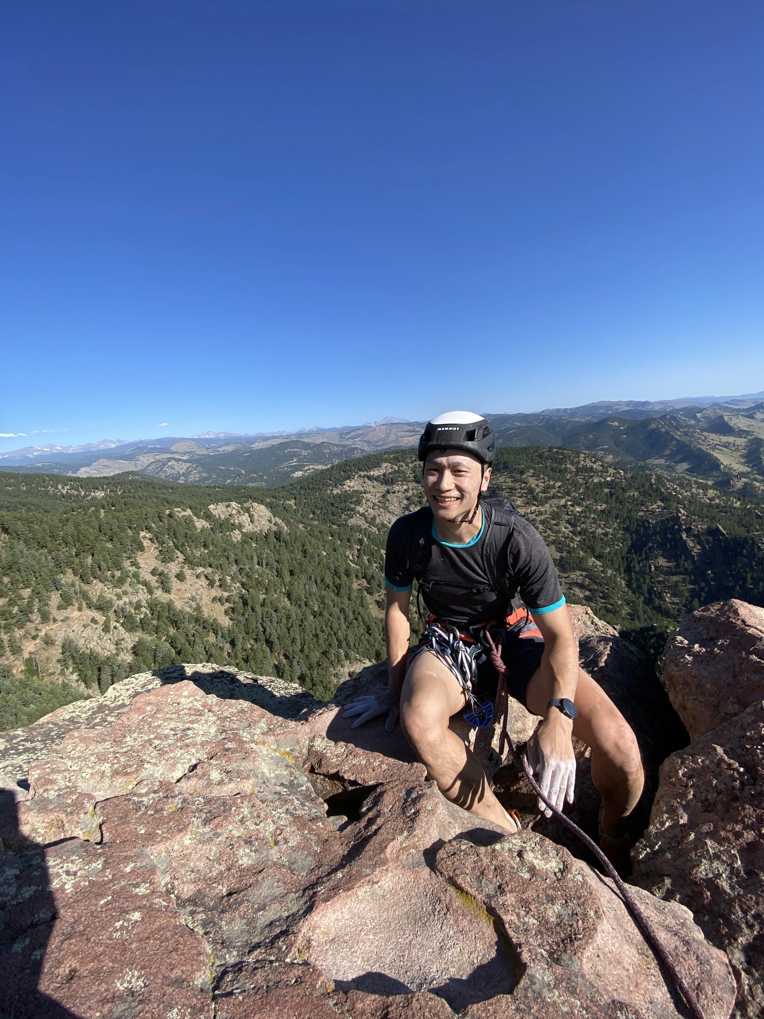 Climber smiling high above Boulder with the Rocky Mountains visible behind