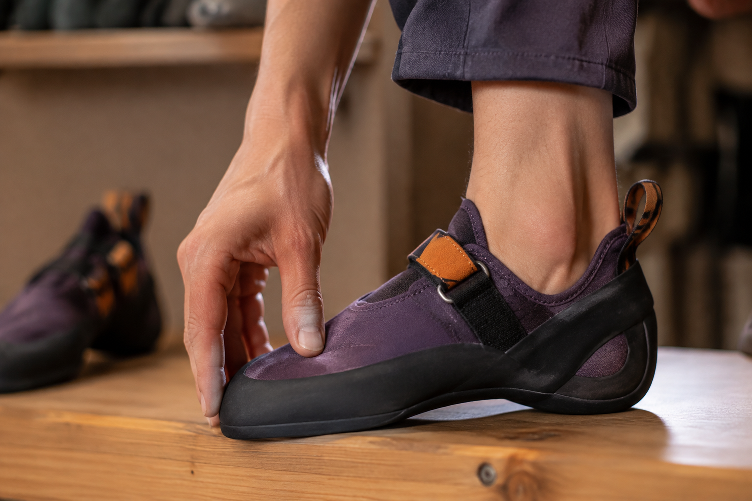 Close-up of a beginner checking the toe and heel fit of a snug purple climbing shoe