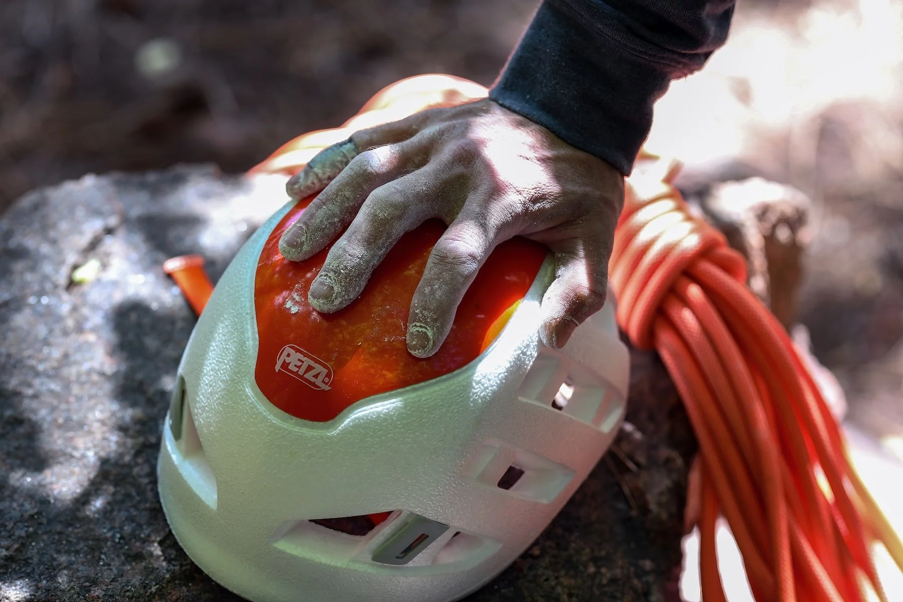 Orange climbing rope tied in a knot, with climbing devices and a carabiner on a dark surface