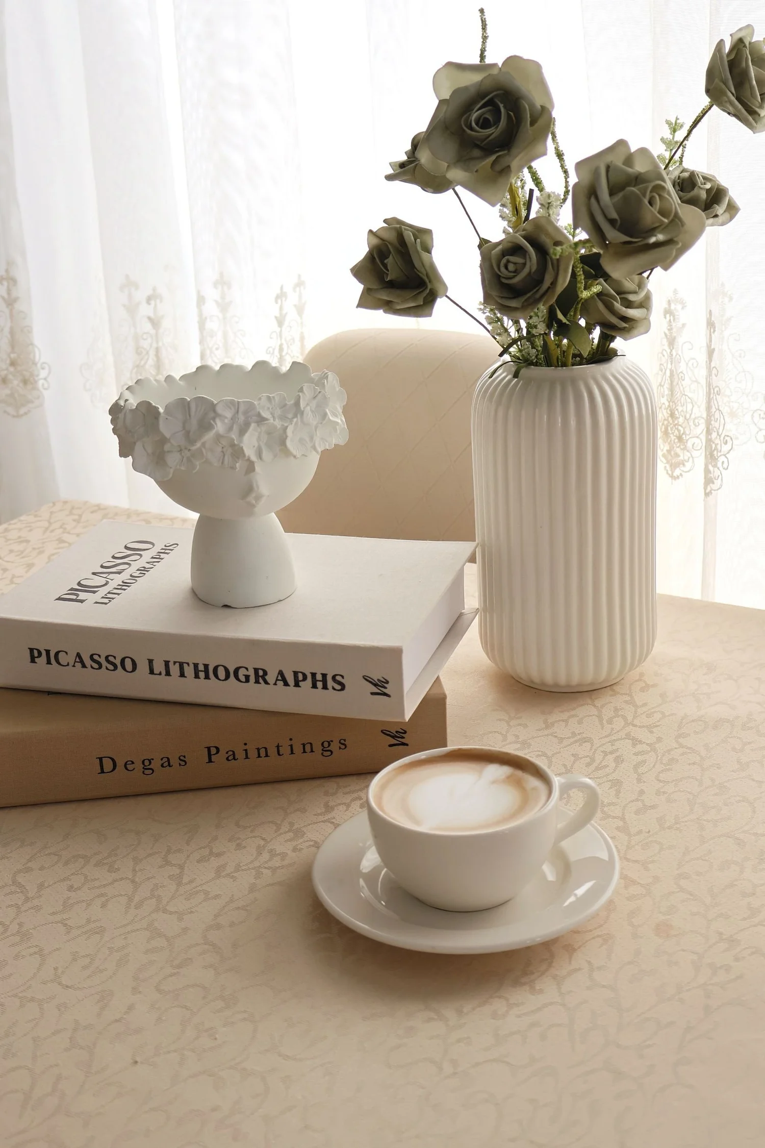A cup of coffee with books and roses beside a lace curtain