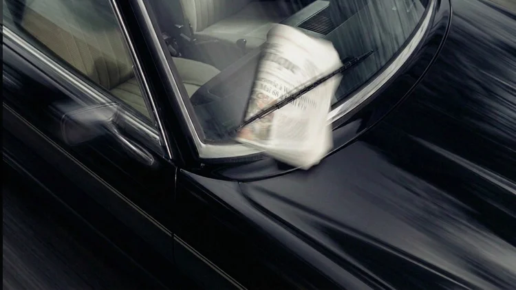 A folded newspaper caught under the windscreen wiper of a black classic car in motion, for BCLR's luxury print design service