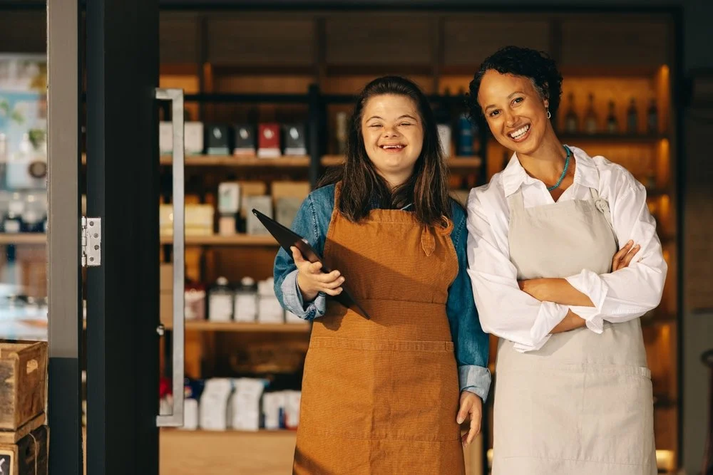 A woman with Down syndrome and a coworker welcoming customers at a café