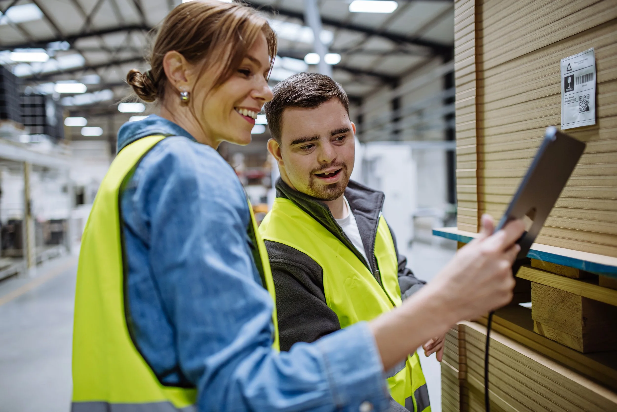 Two coworkers in safety vests reviewing information on a tablet in a warehouse