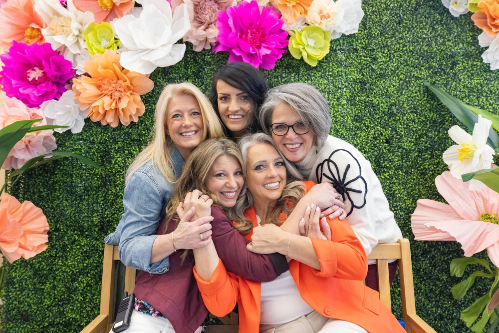 Friends embracing at the MORE 2025 flower wall