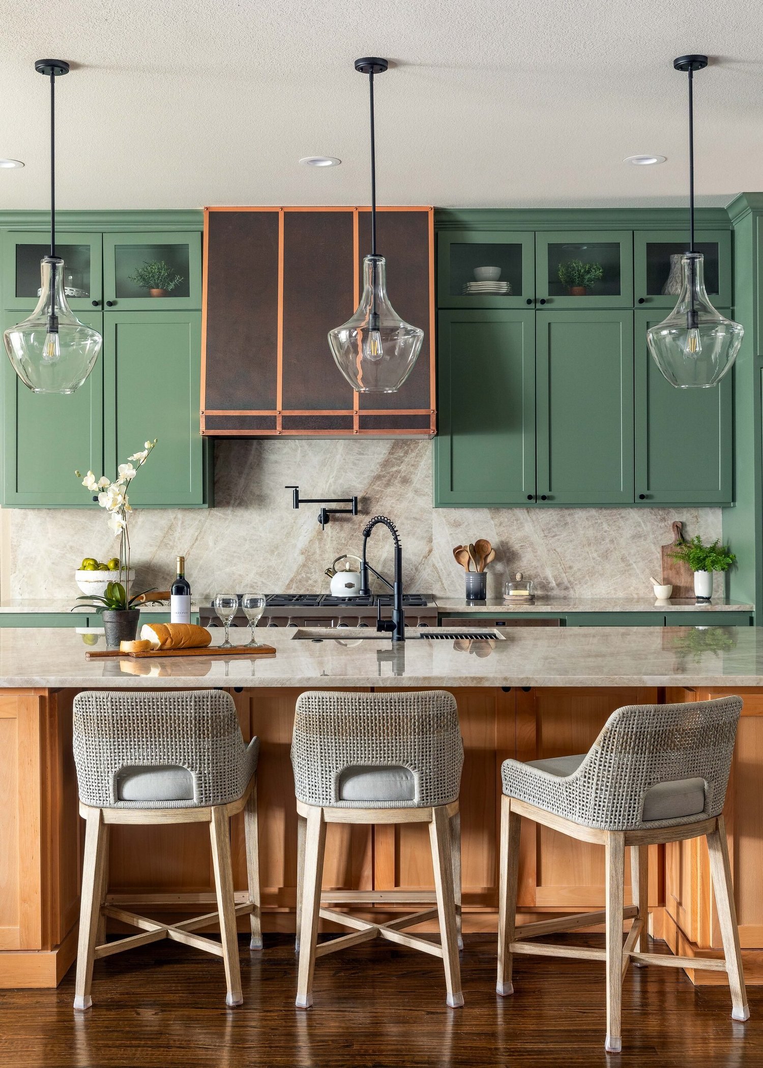 Sage green kitchen with glass pendants over a wood island and quartzite counters