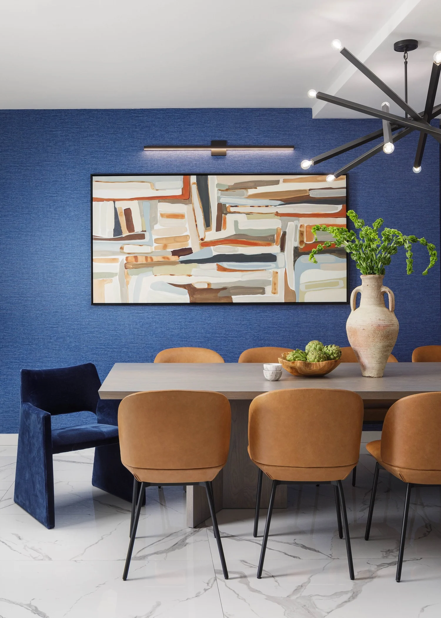 Dining table with cognac chairs and a navy host chair beneath a large abstract painting