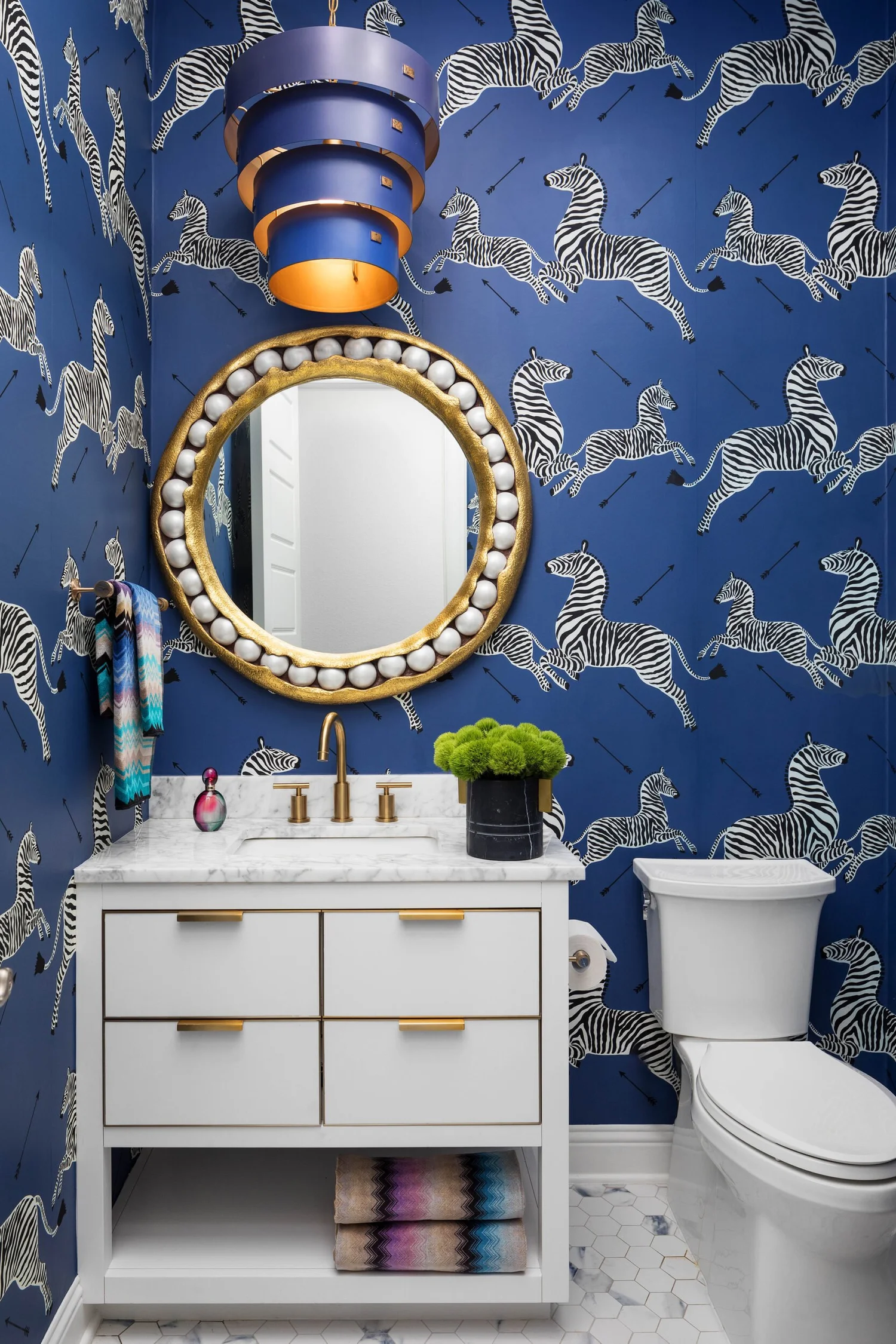 Powder bath with blue zebra wallpaper, a white vanity and a round gold mirror