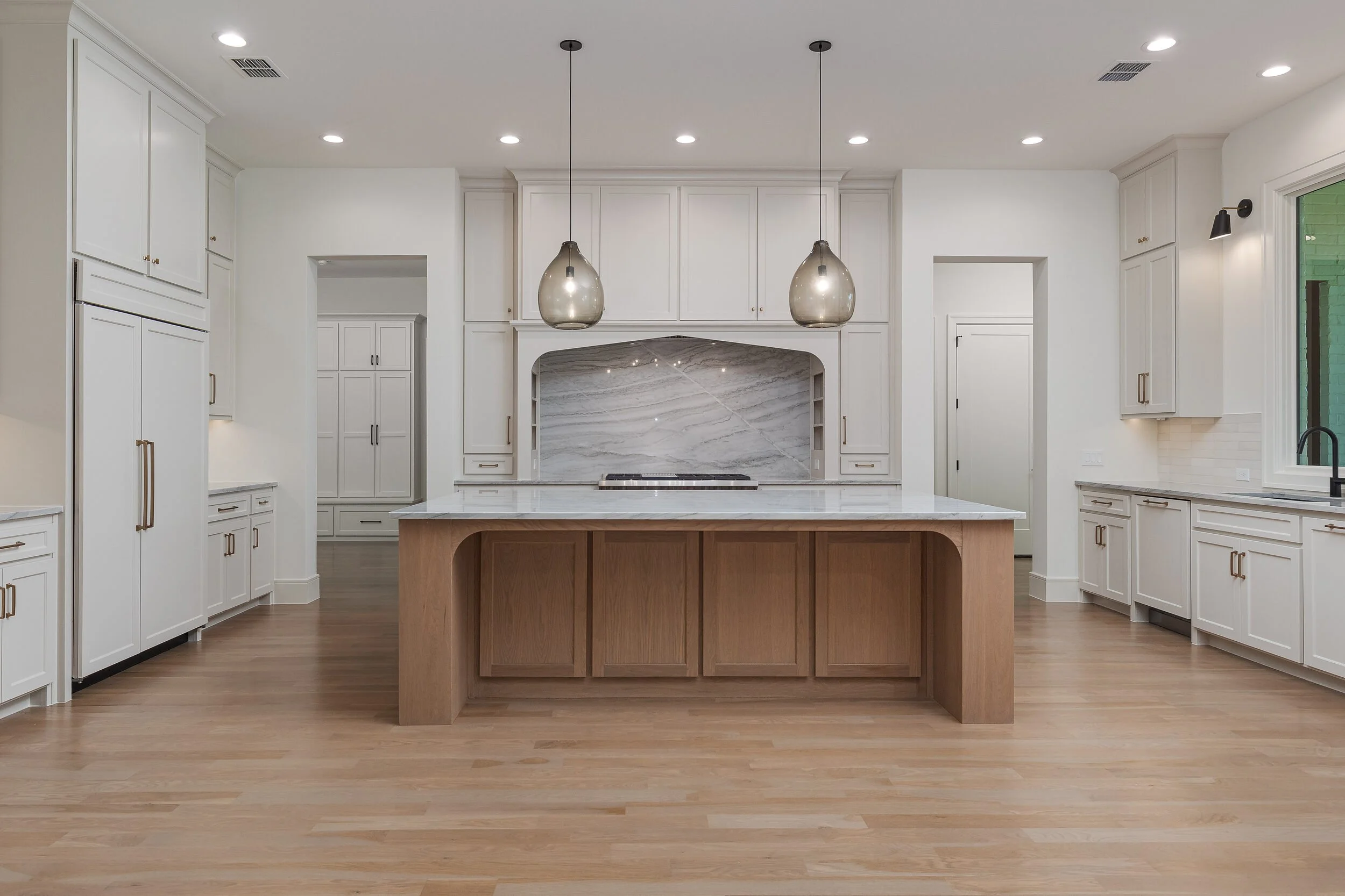 Kitchen with a white oak island, glass pendants and a tiled range hood alcove