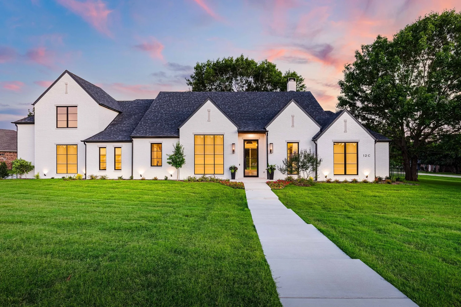 White brick custom home at twilight with lit windows and a long front walk, built by Jesse Adams Custom Homes