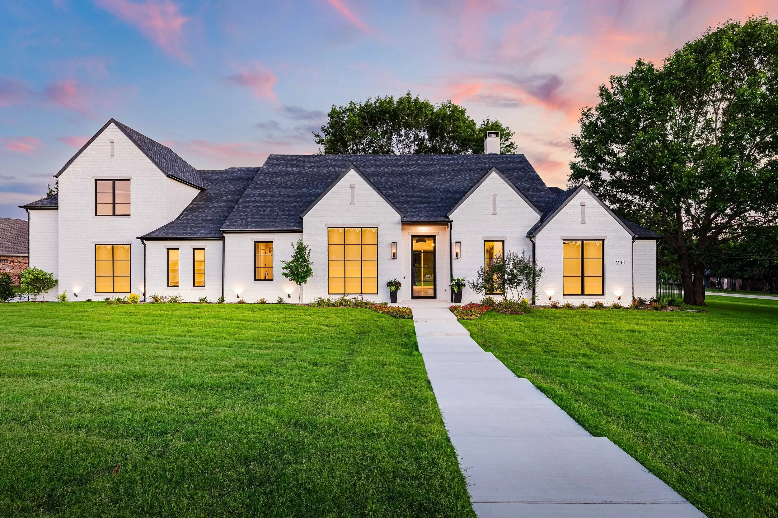 White brick custom home at twilight with lit windows and a long front walk, built by Jesse Adams Custom Homes