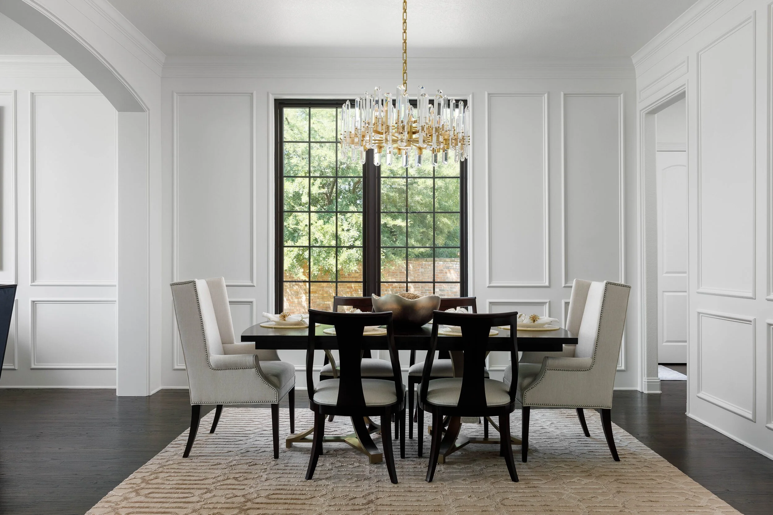 Paneled dining room with a crystal chandelier, black dining chairs and a tall arched window