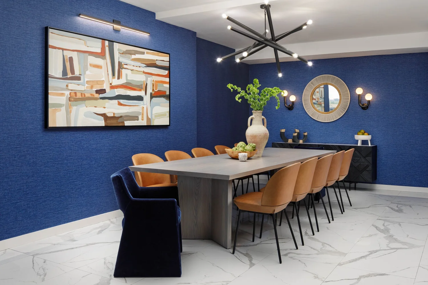 Dining room with a blue grasscloth wall, abstract art and a long table with cognac chairs, designed by Amy Switzer Design