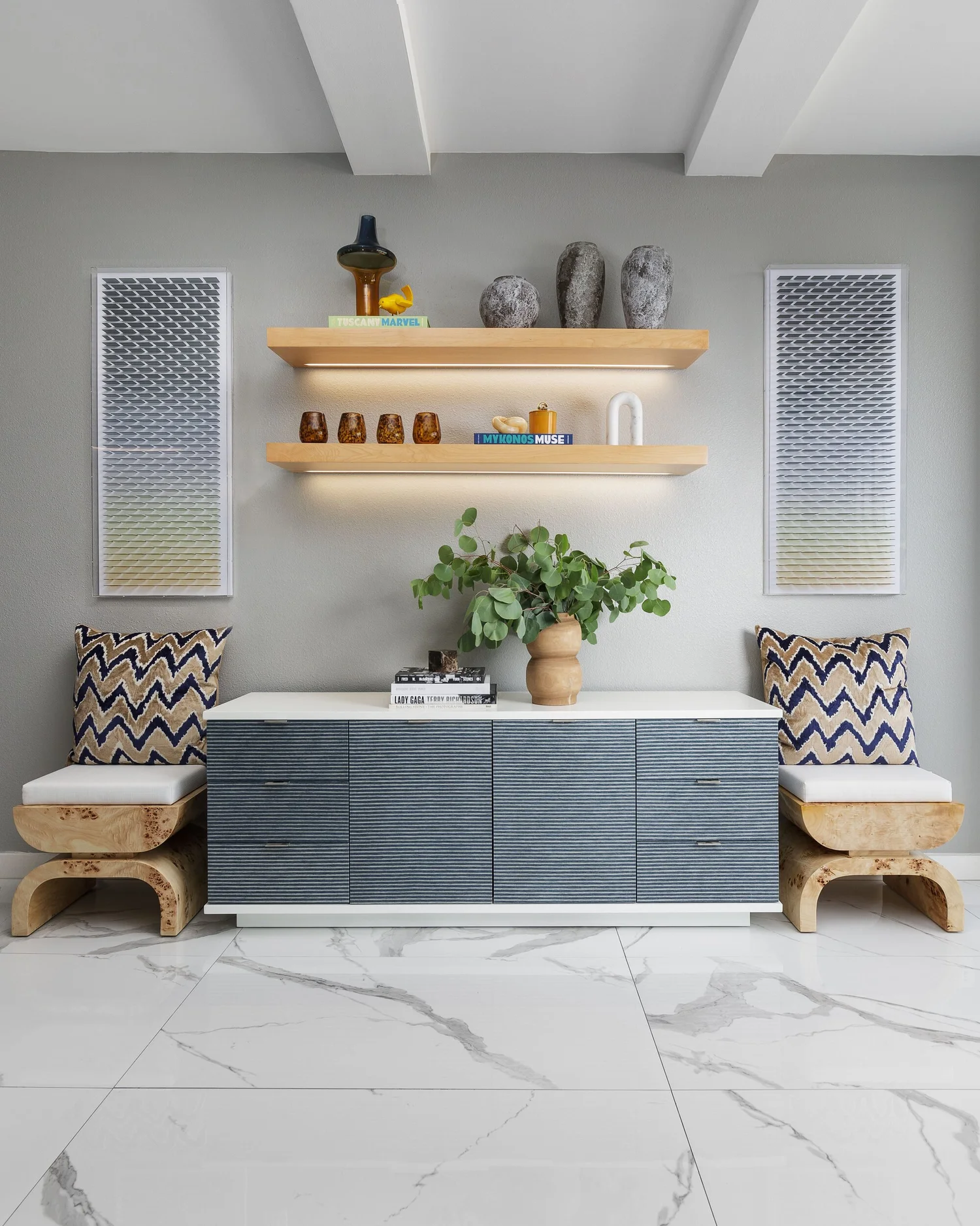 Floating oak shelves above a gray lacquered credenza flanked by two carved stools