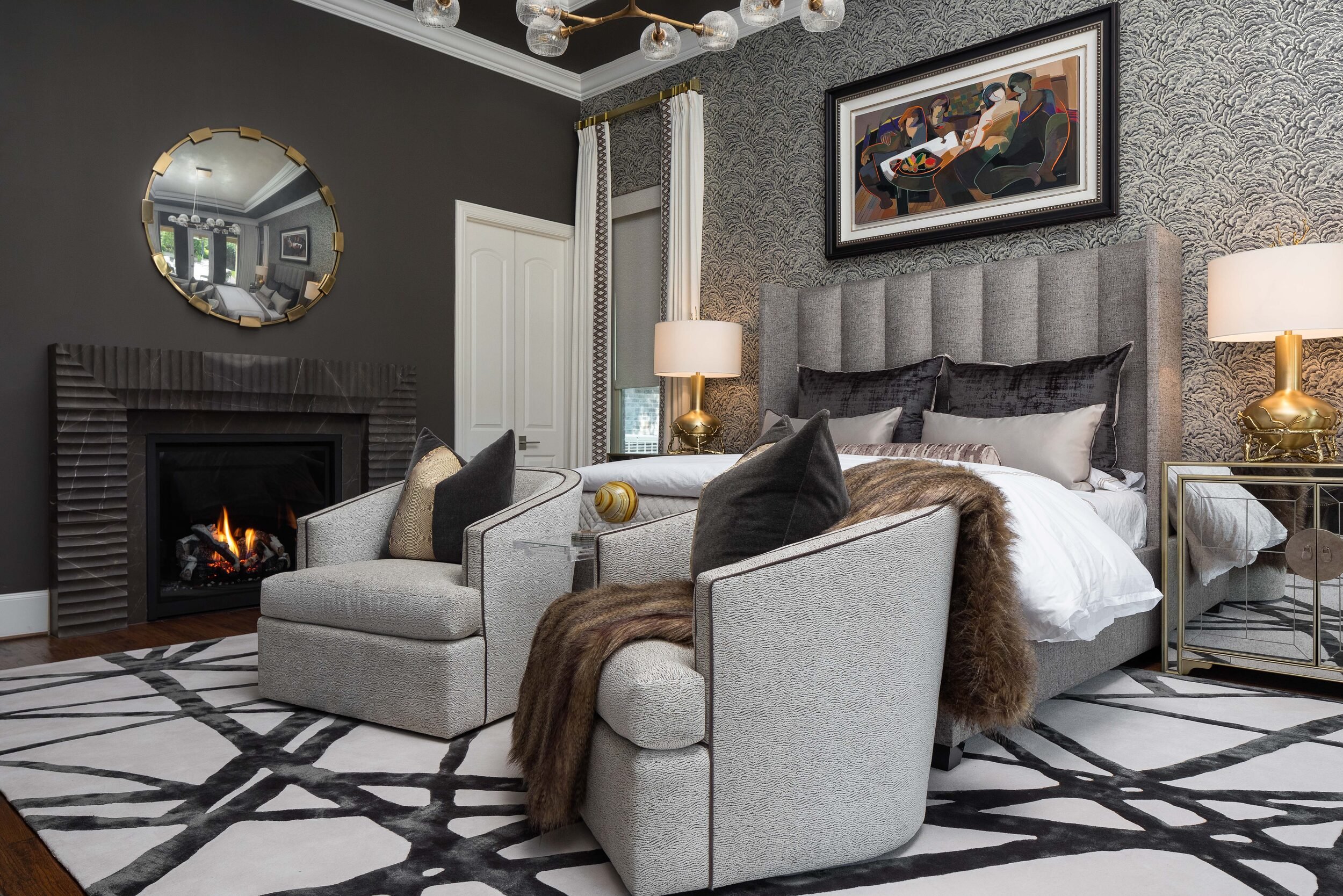 Primary bedroom with a fireplace, round mirror and a pair of upholstered swivel chairs
