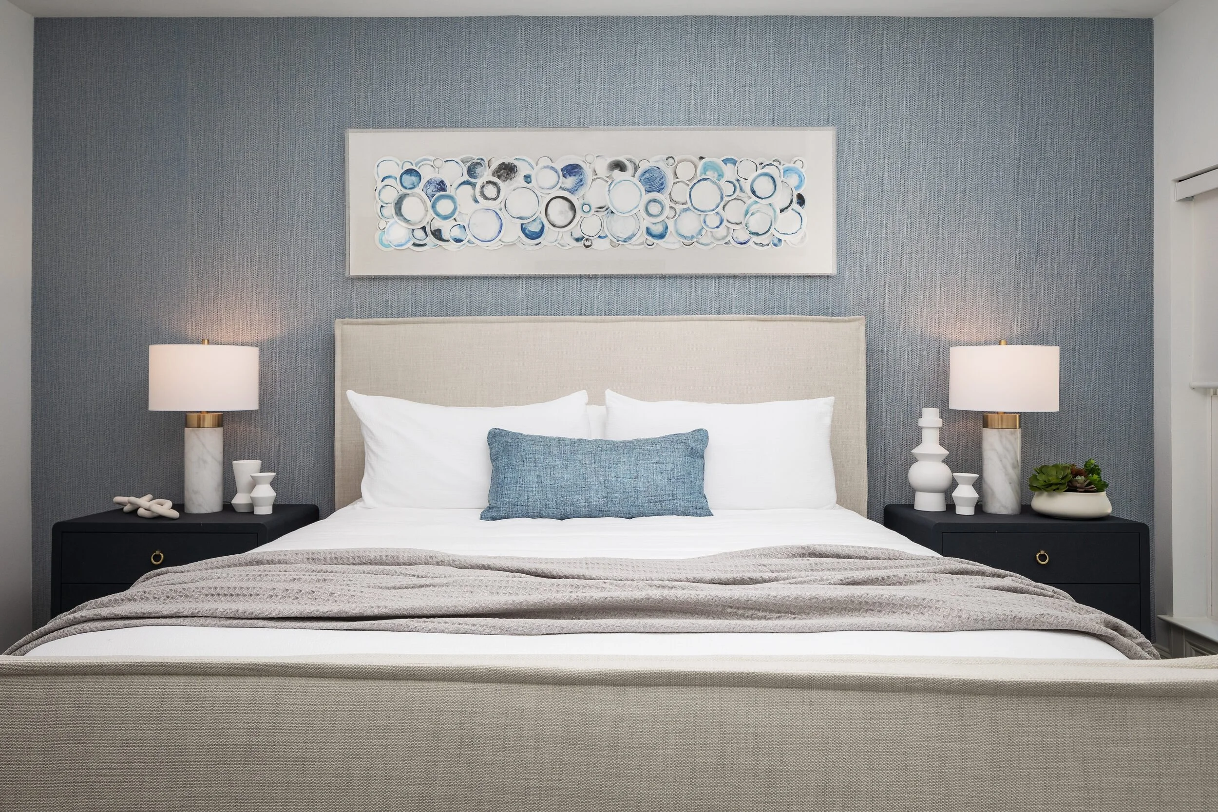 Bedroom with a gray grasscloth wall, a linen upholstered bed and circle-pattern art