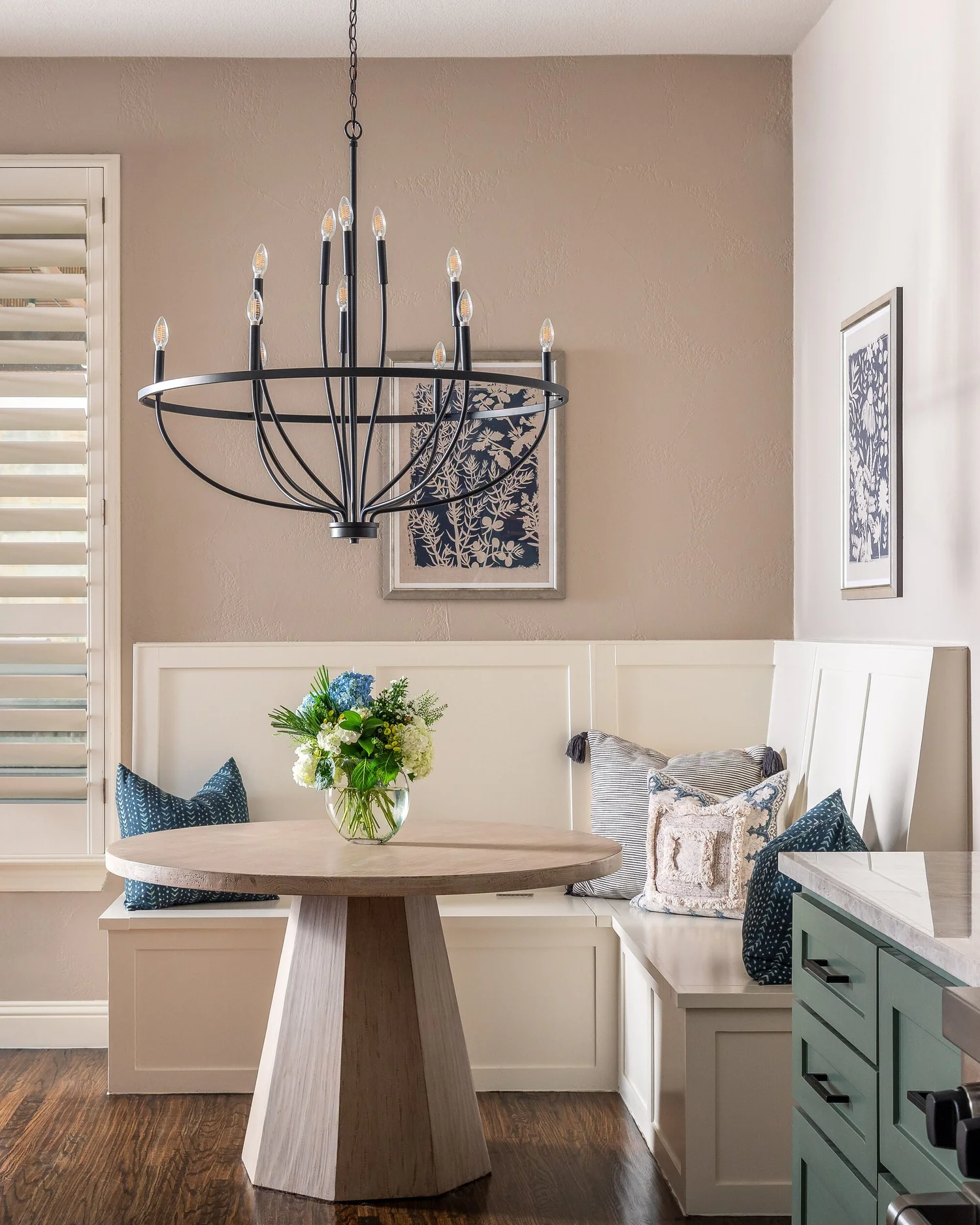 Breakfast nook with a round pedestal table, banquette pillows and an iron chandelier