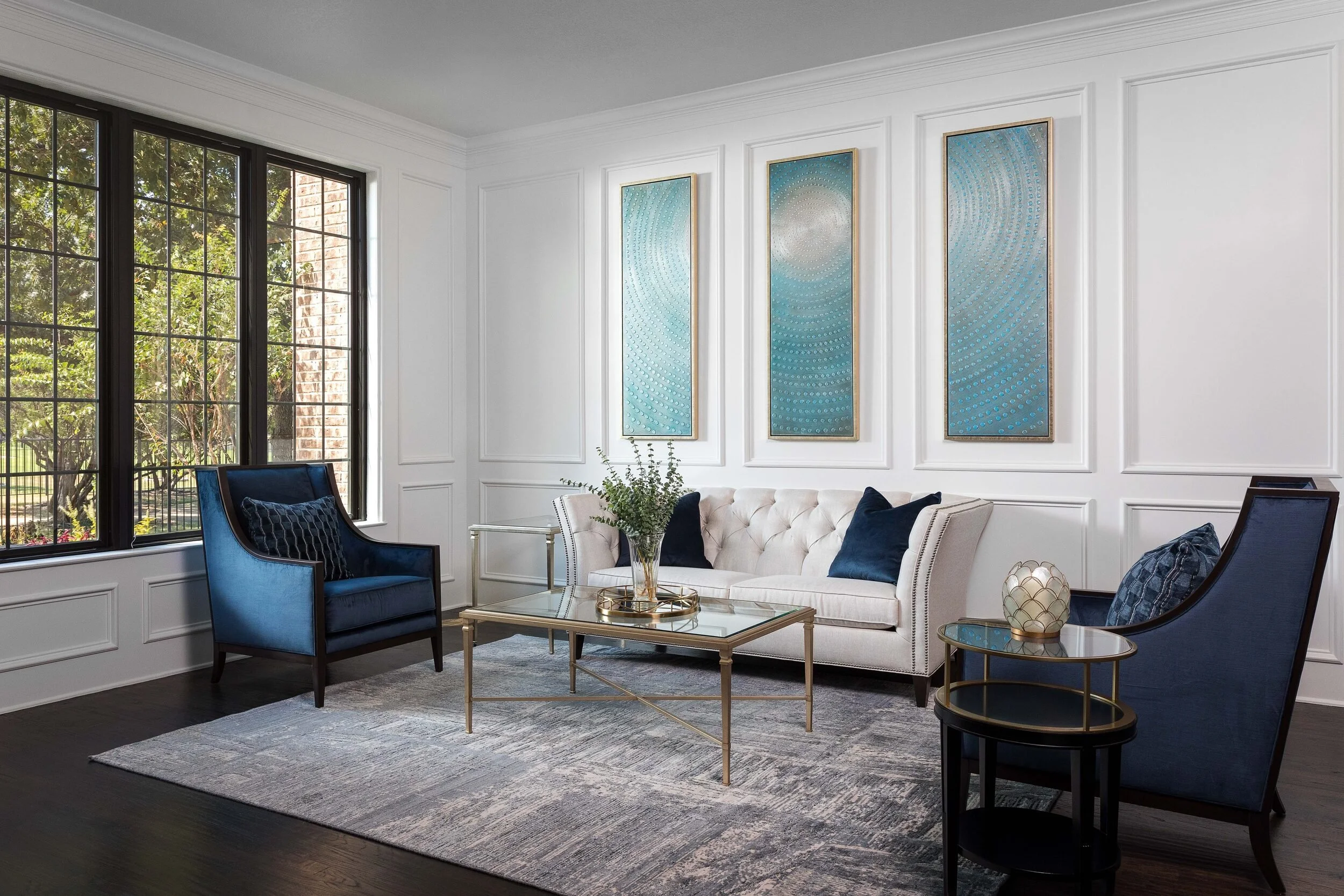 Sitting room with paneled walls, a tufted sofa, navy accent chairs and a triptych of blue art