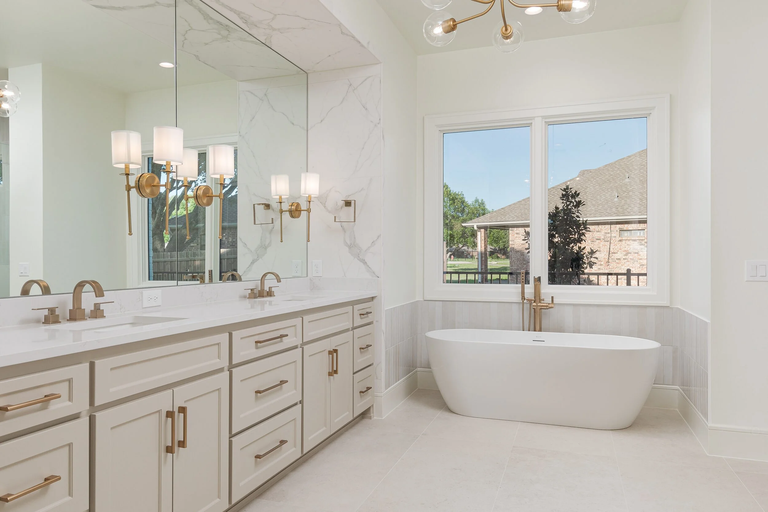 Primary bath with a freestanding tub, brass sconces and a double vanity
