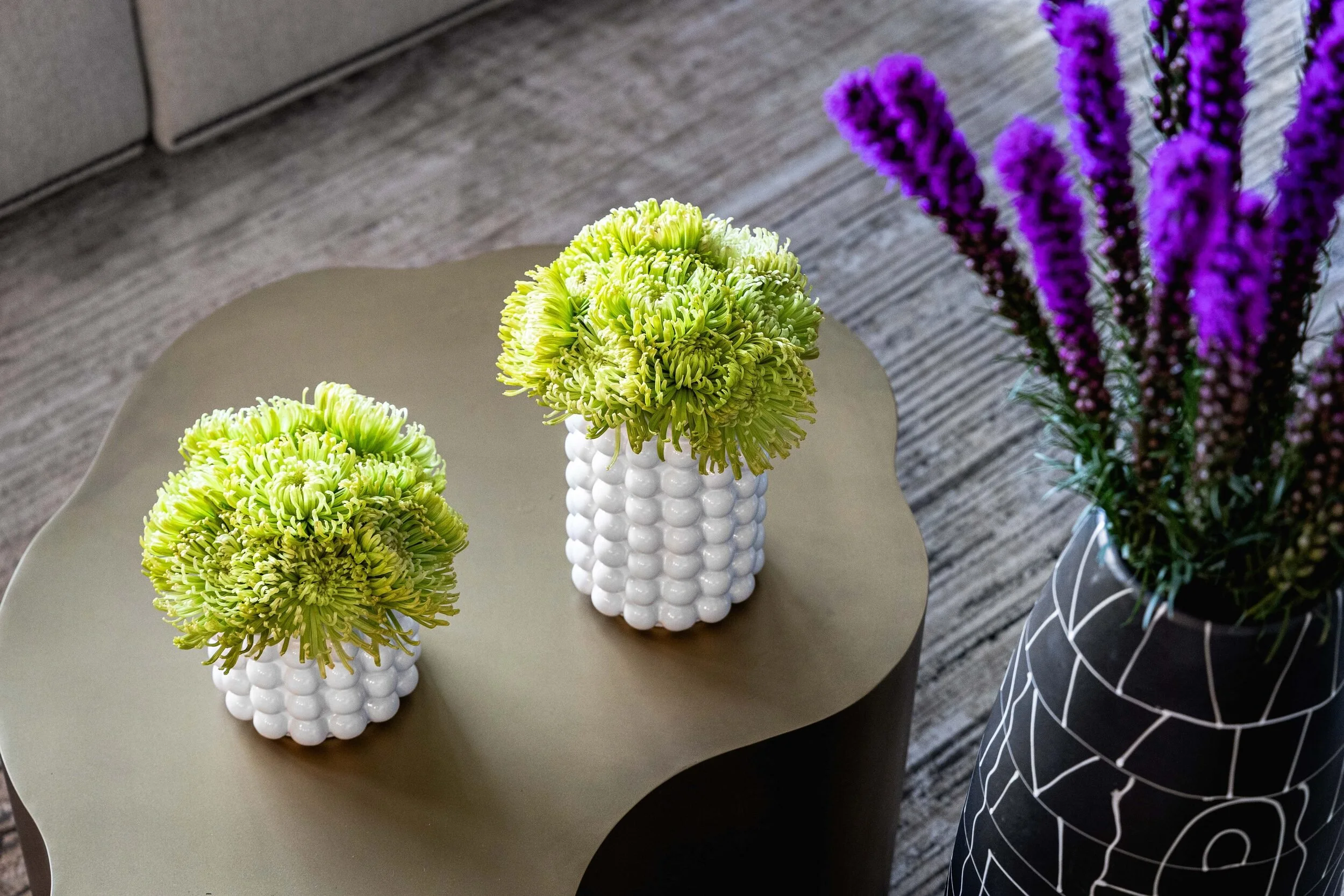 Detail of a sculptural bronze coffee table with white beaded planters and purple stems