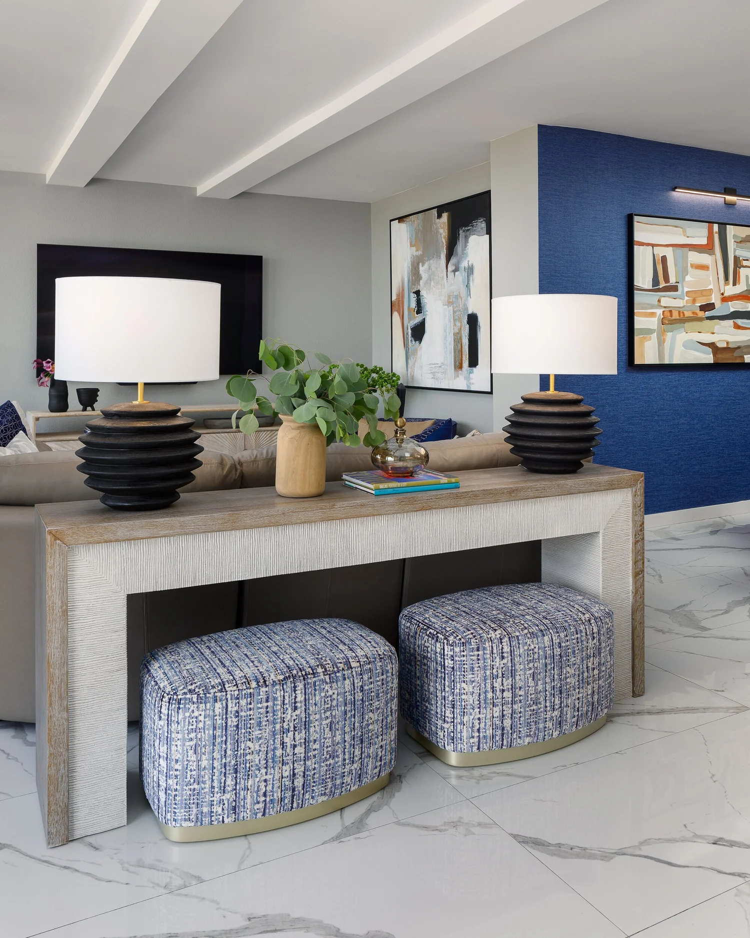 Sofa console with black ceramic lamps and two woven ottomans tucked beneath