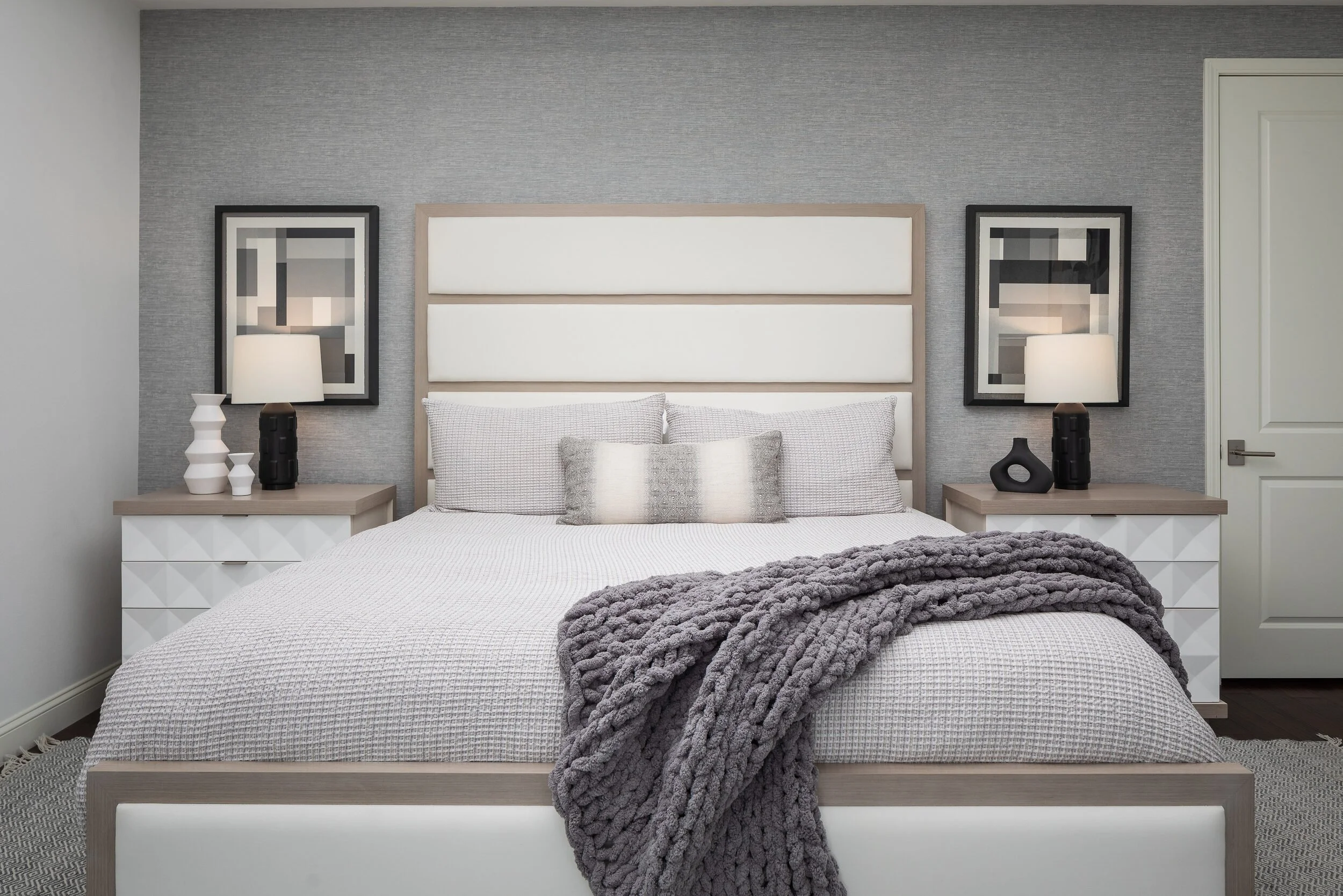 Bedroom with a gray grasscloth wall, a white paneled headboard and a charcoal knit throw