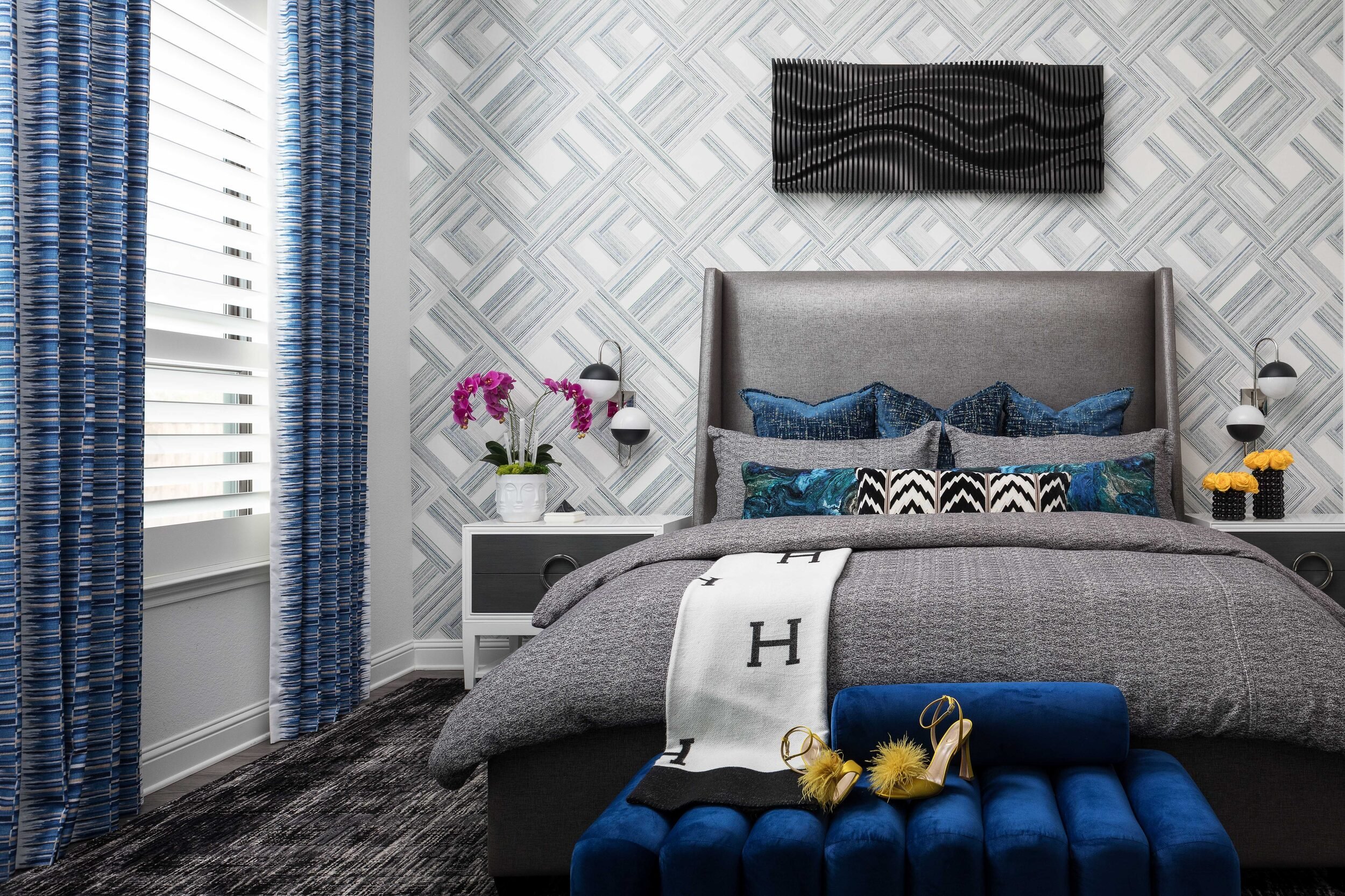 Straight-on view of the primary bed with a blue velvet bench and geometric wallpaper