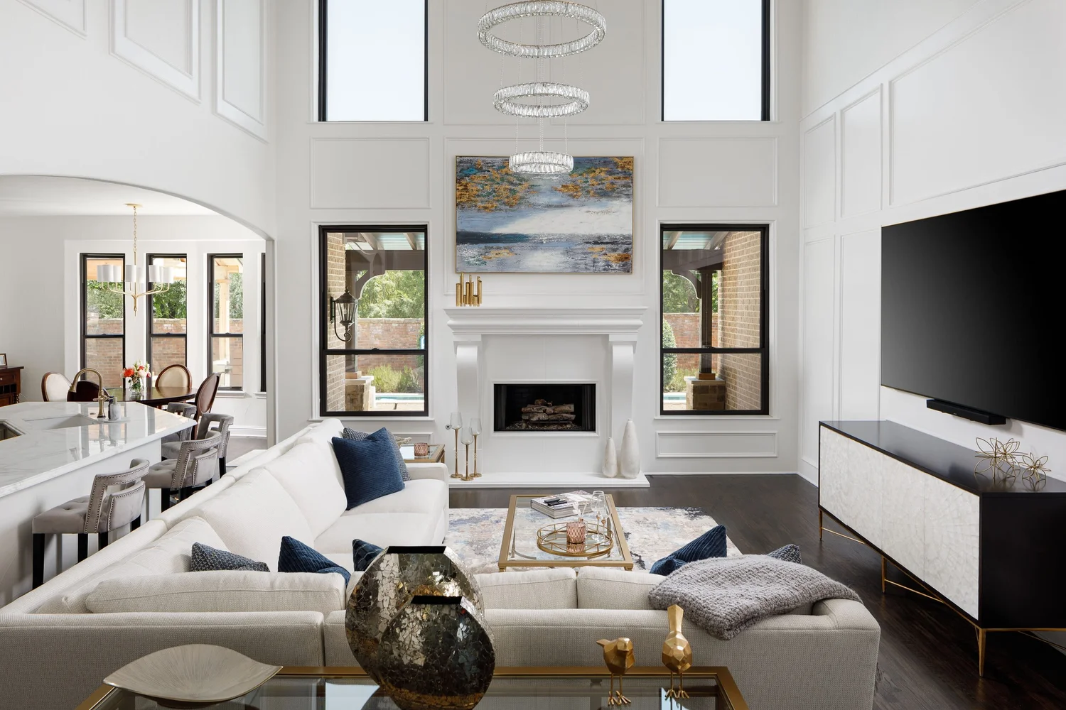 Two-story living room with white paneled walls, a cast stone fireplace and navy accents, by Agapé Home Services