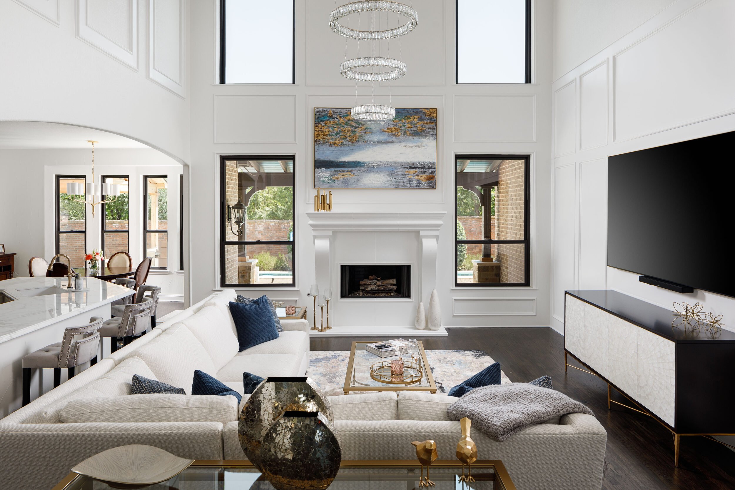 Two-story living room with white paneled walls, a cast stone fireplace and navy accents, by Agapé Home Services