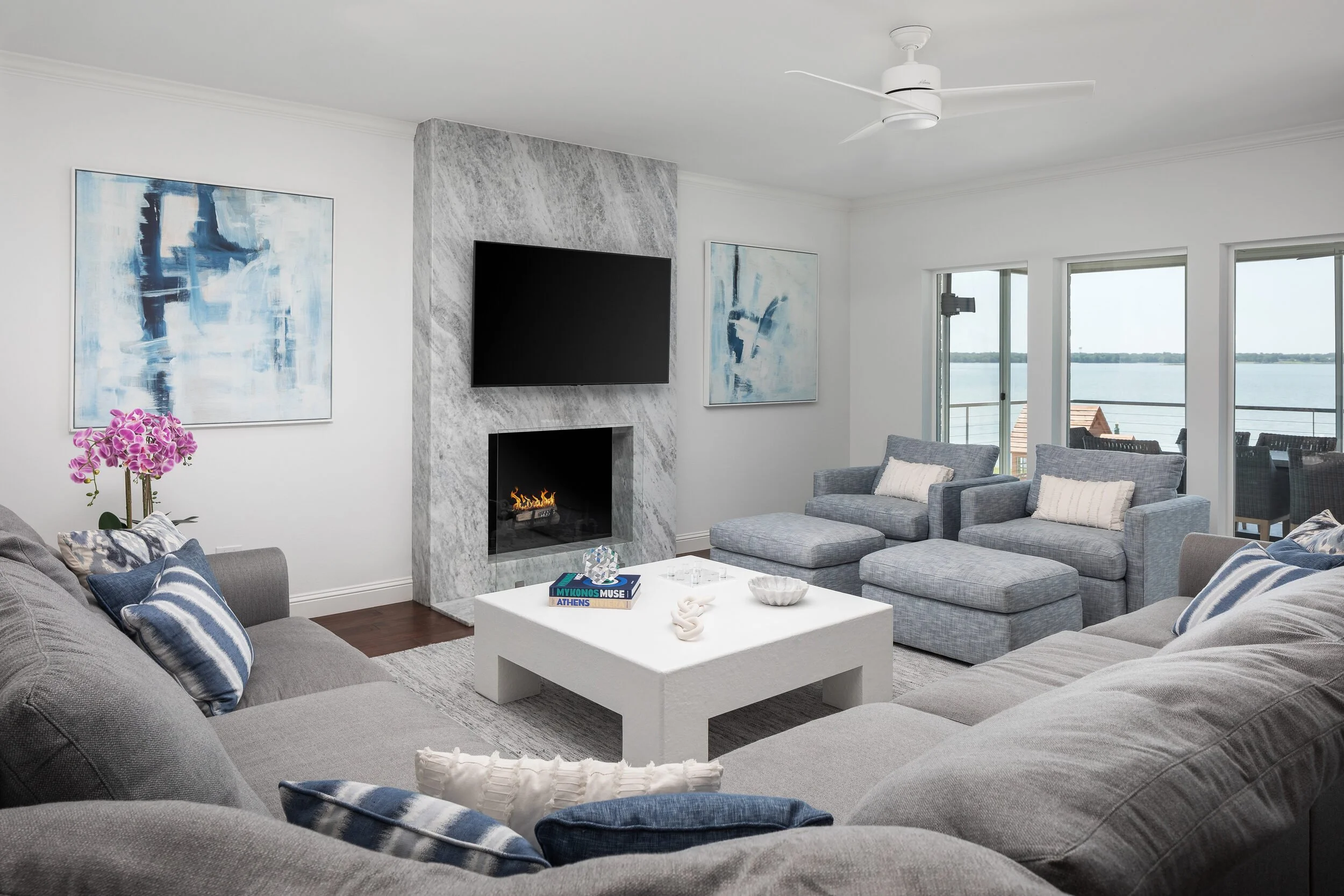 Living room with a gray sectional, white coffee table and a marble fireplace wall, with lake views through the windows
