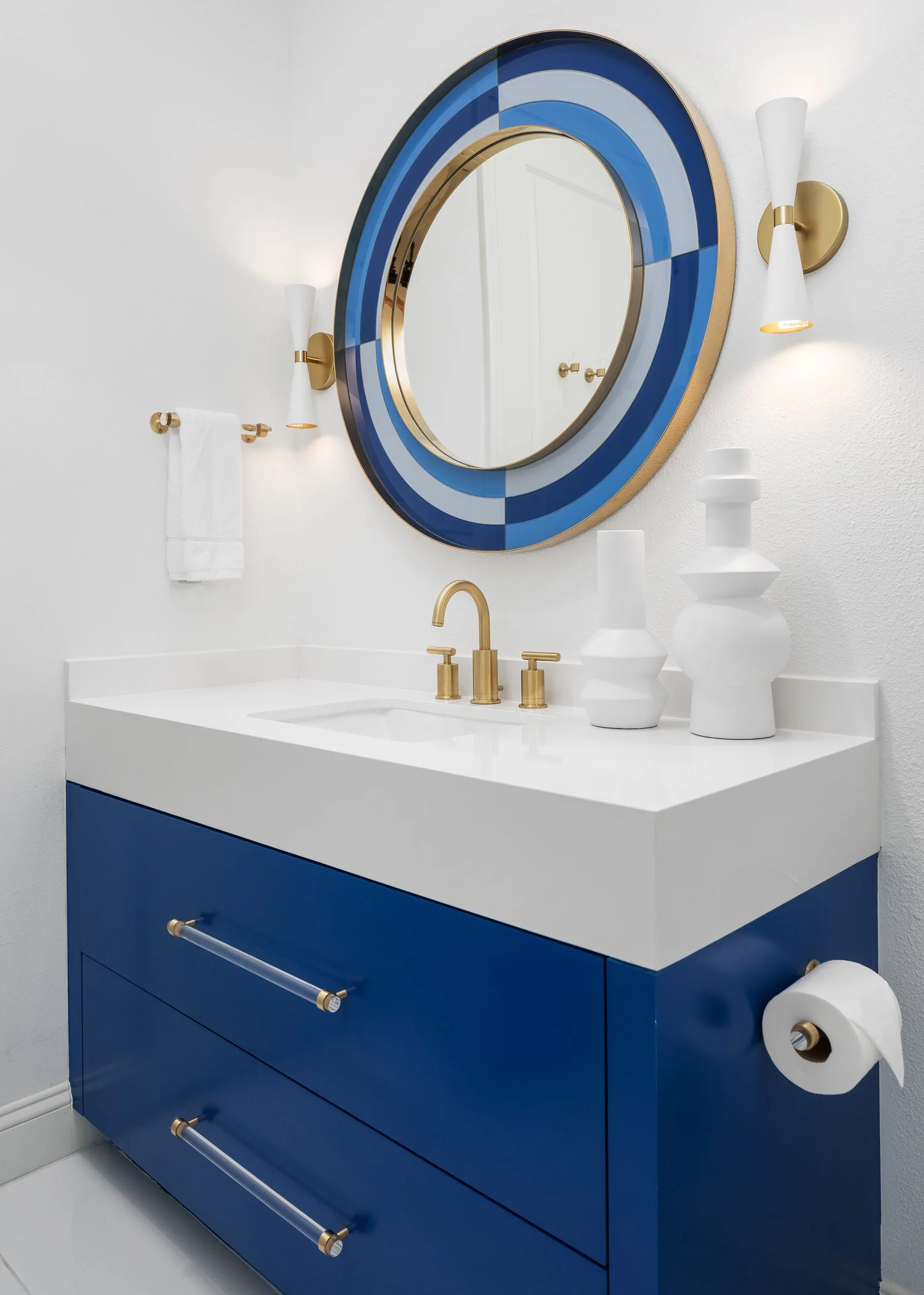 Guest bath with a navy vanity below a round blue mirror and brass sconce