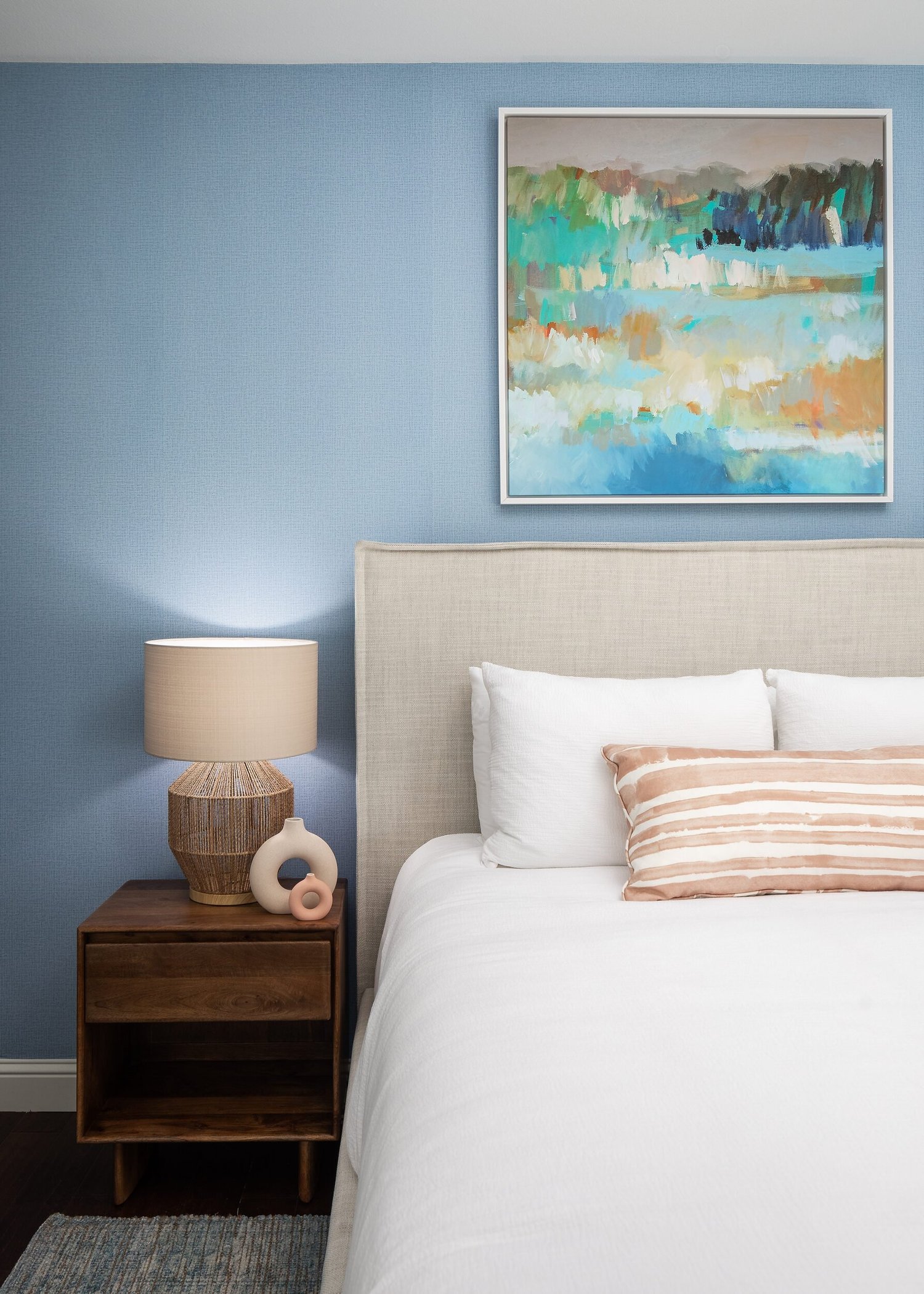 Bed against a powder blue wall with a landscape painting and woven lamps
