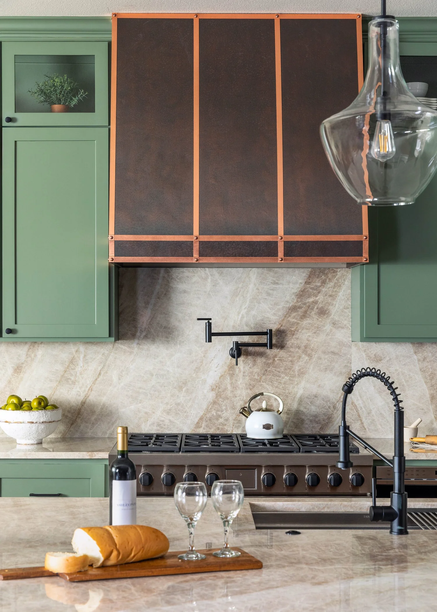 Detail of a dark metal range hood with copper trim above a pot filler