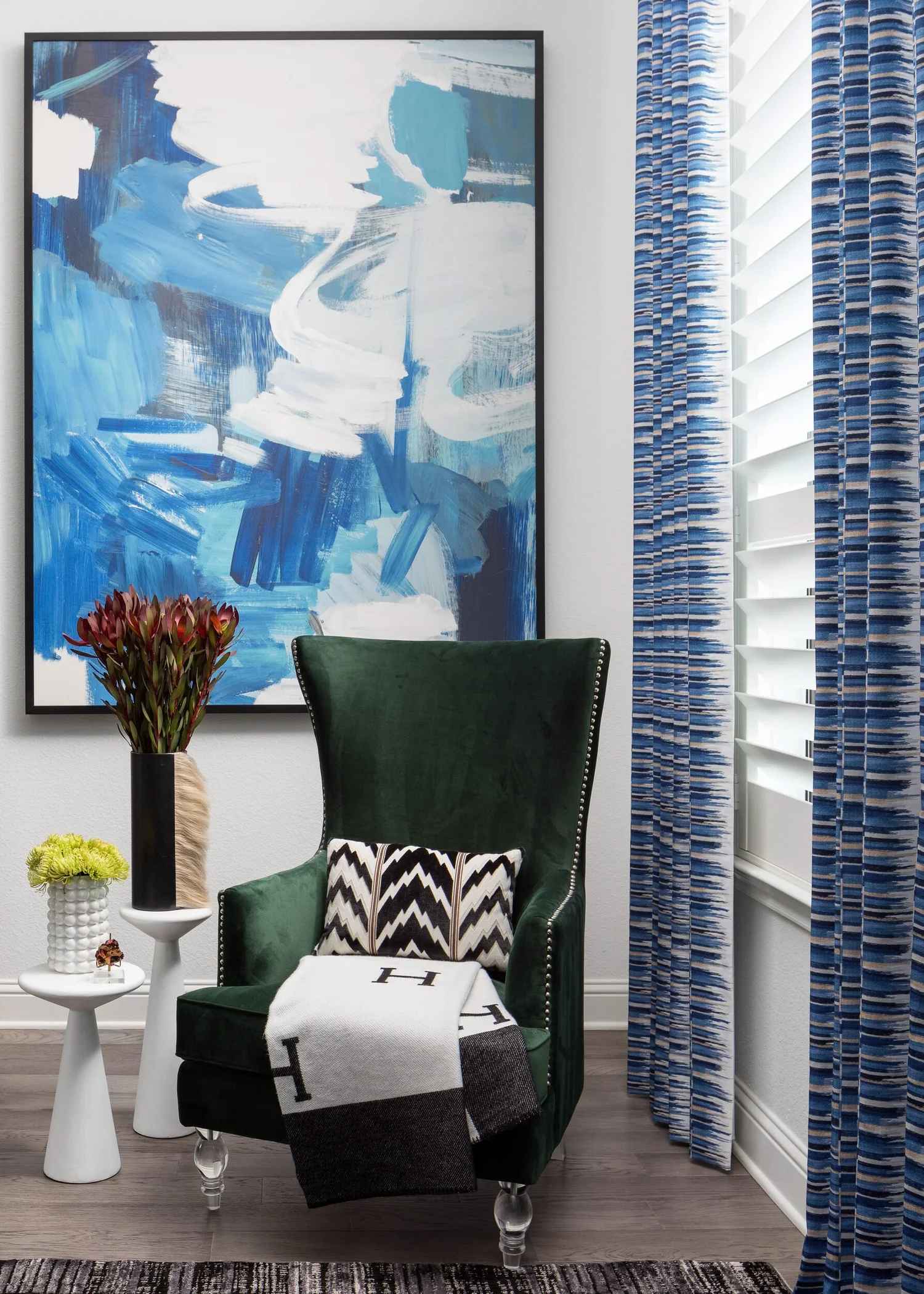 Green velvet wingback chair below a large blue abstract painting in the primary bedroom